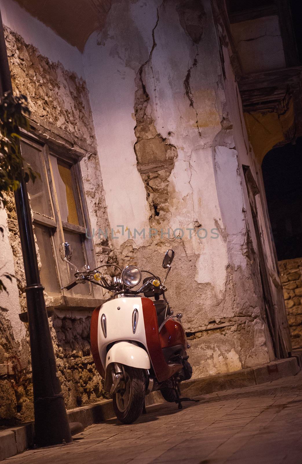 White vintage scooter parked at night in narrow old street of Antalya, Turkey