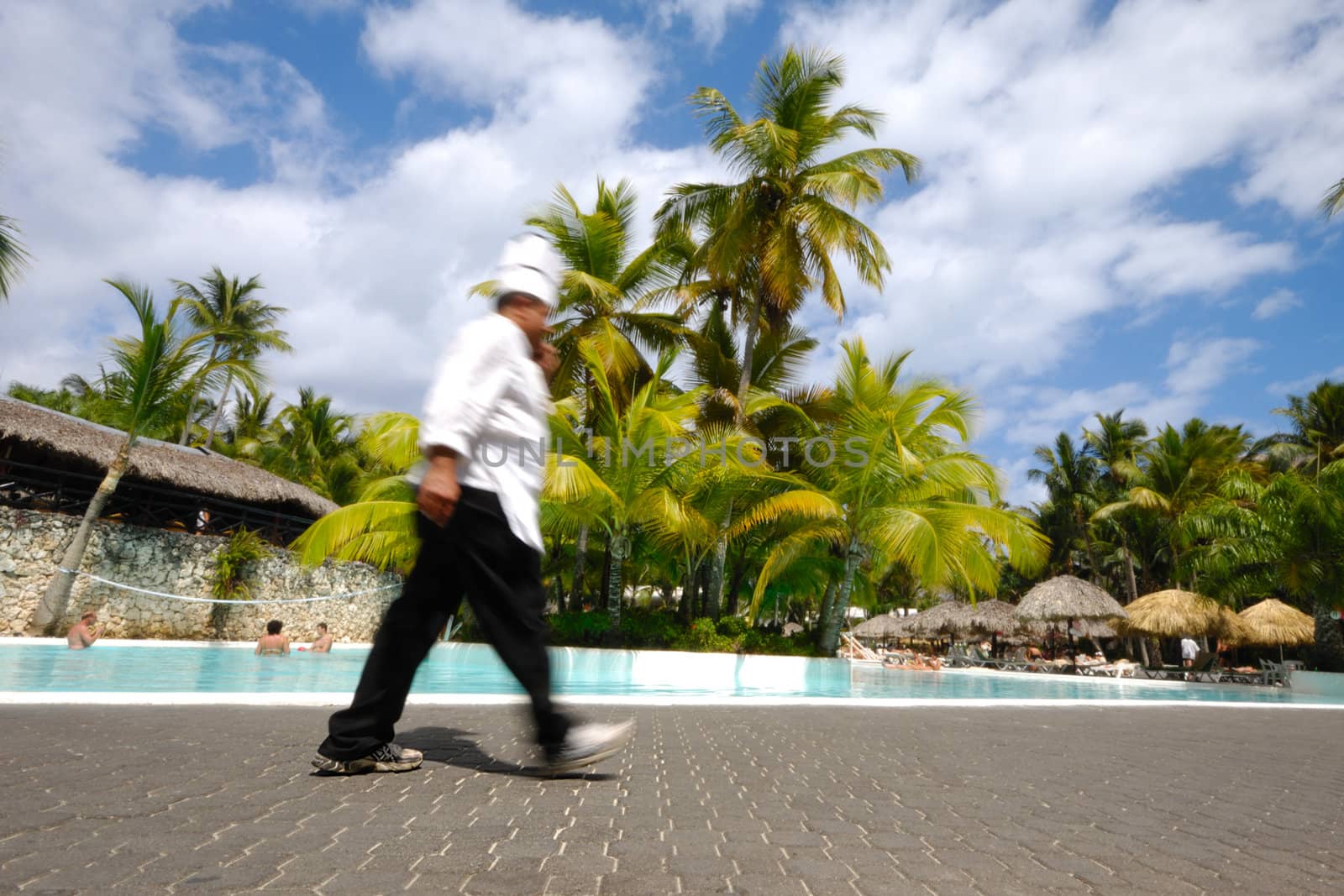 Chef is walking by nice swimming pool on his way to work. Motion blur.