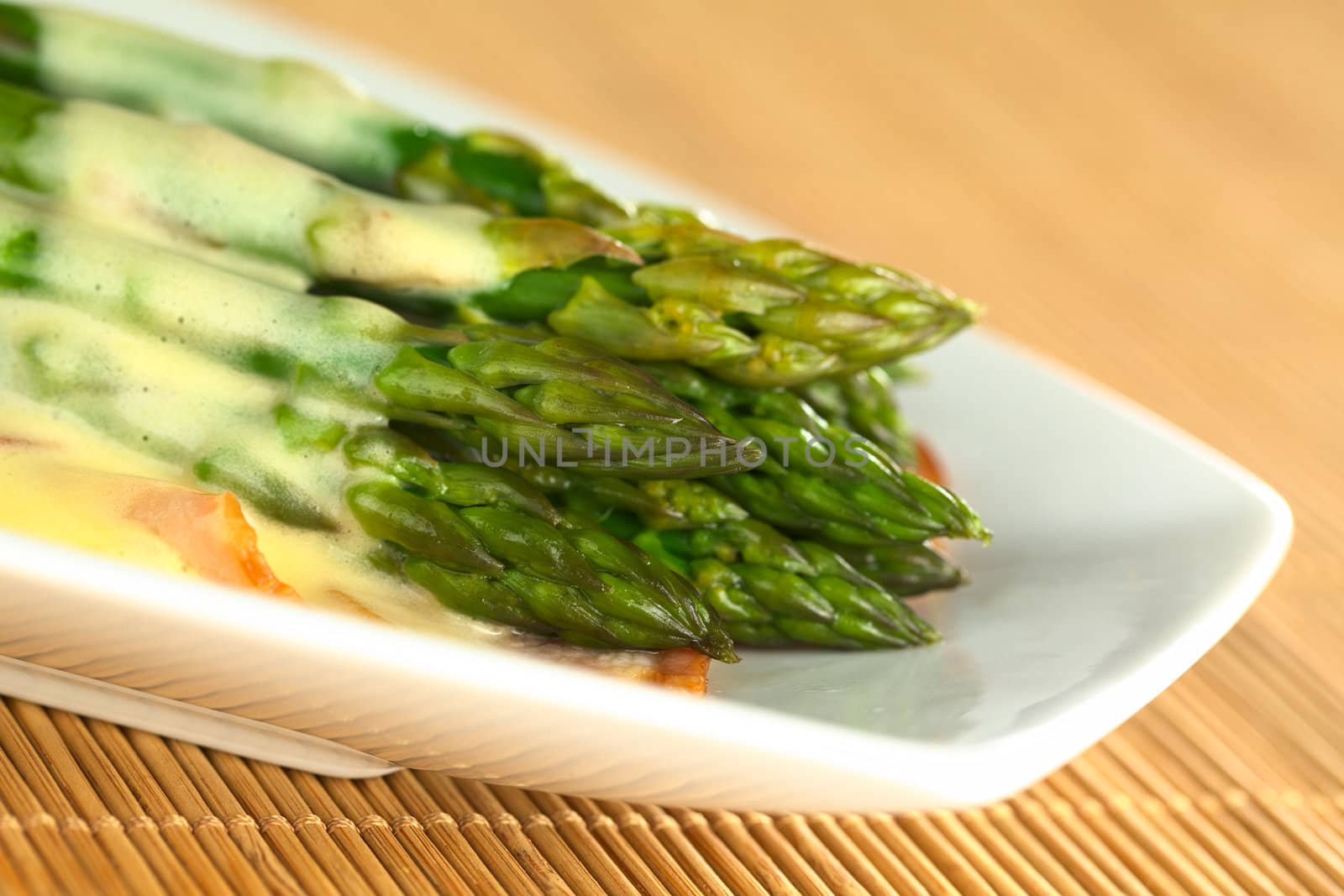 Cooked green asparagus on fried bacon with Hollandaise sauce on top (Selective Focus, Focus on the two asparagus tips in the front)