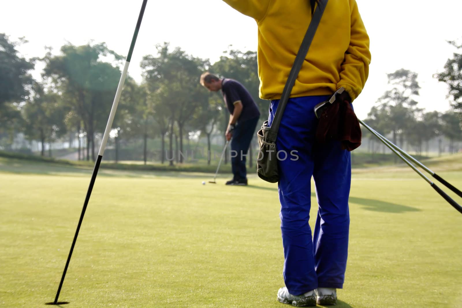 Caddie tending the pin as golfer lines up a putt