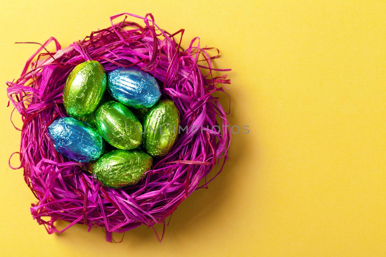 Easter chocolate eggs in pink nest. Holiday composition on yellow paper background. Top view
