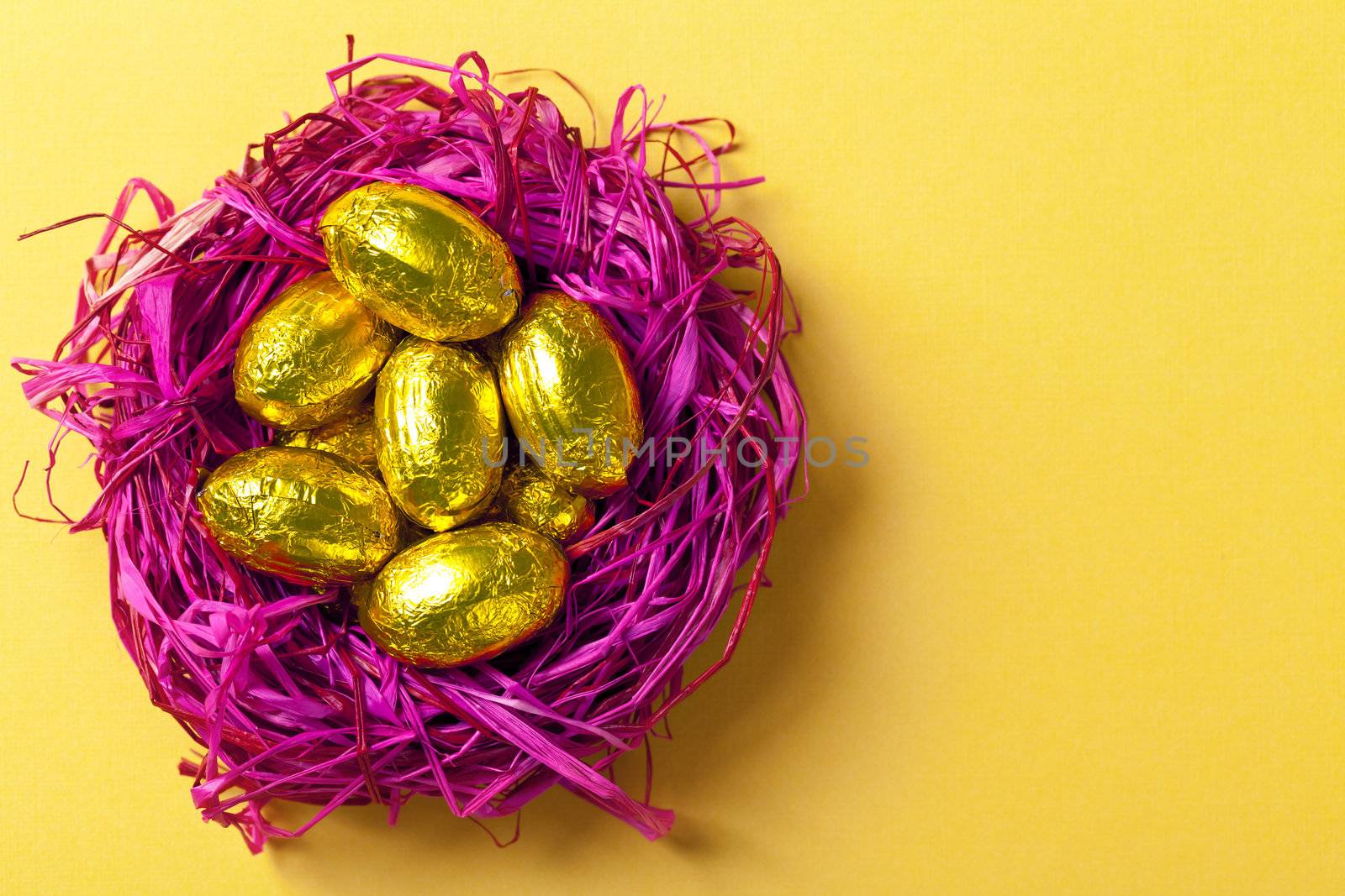 Chocolate easter eggs in pink nest. Holiday composition on yellow paper background. Top view. Macro shot
