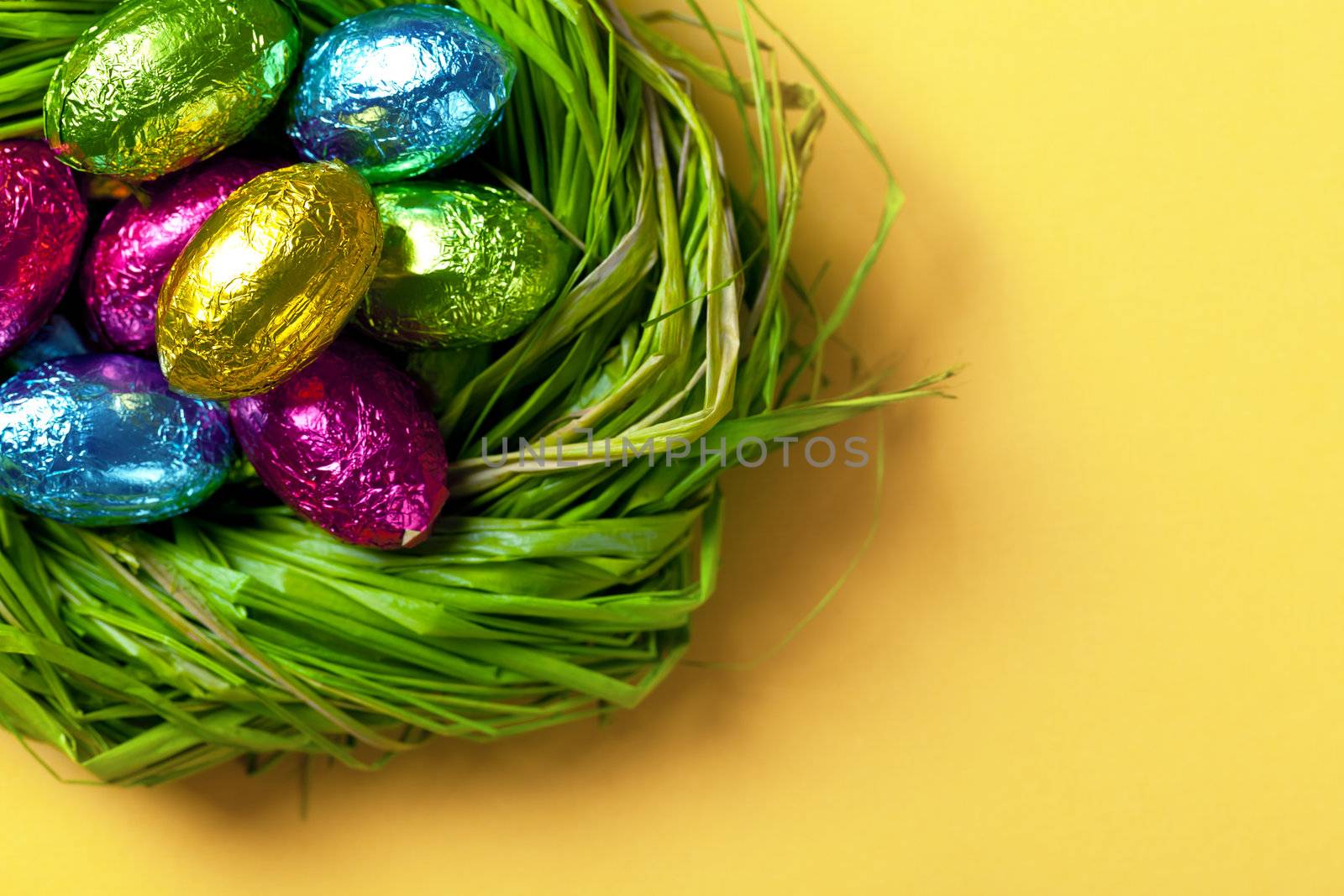 Colorful easter eggs in green nest. Holiday chocolate background. Top view. Macro shot