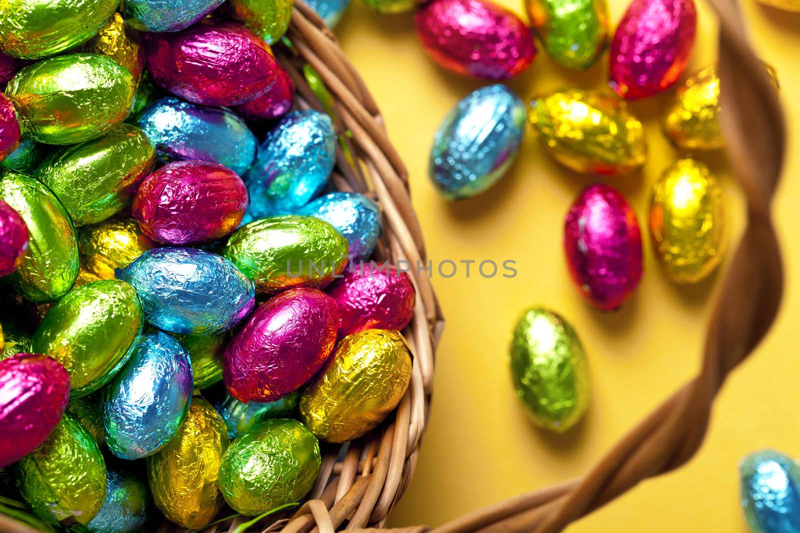Easter basket with colorful chocolate eggs on yellow paper background, Top view. Macro shot