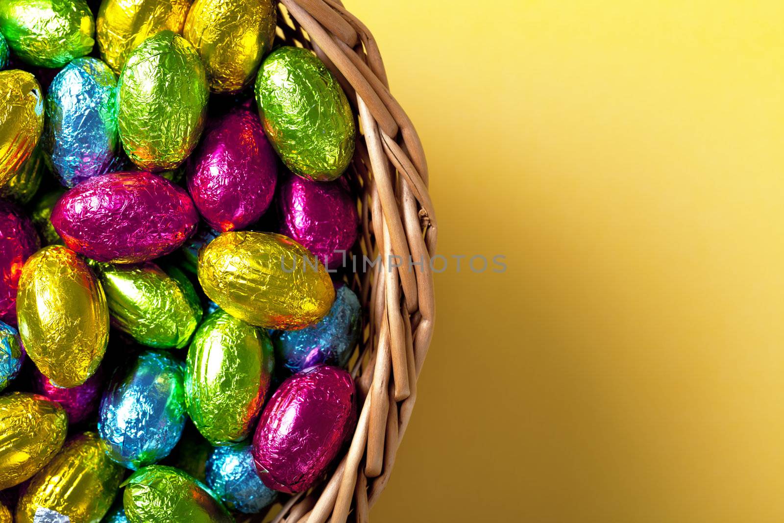 Easter basket with chocolate eggs on yellow paper background, Top view. Macro shot 