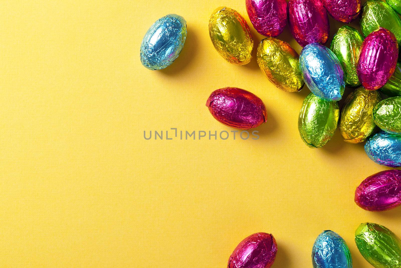 Colorful chocolate easter eggs on yellow paper background. Top view, macro shot