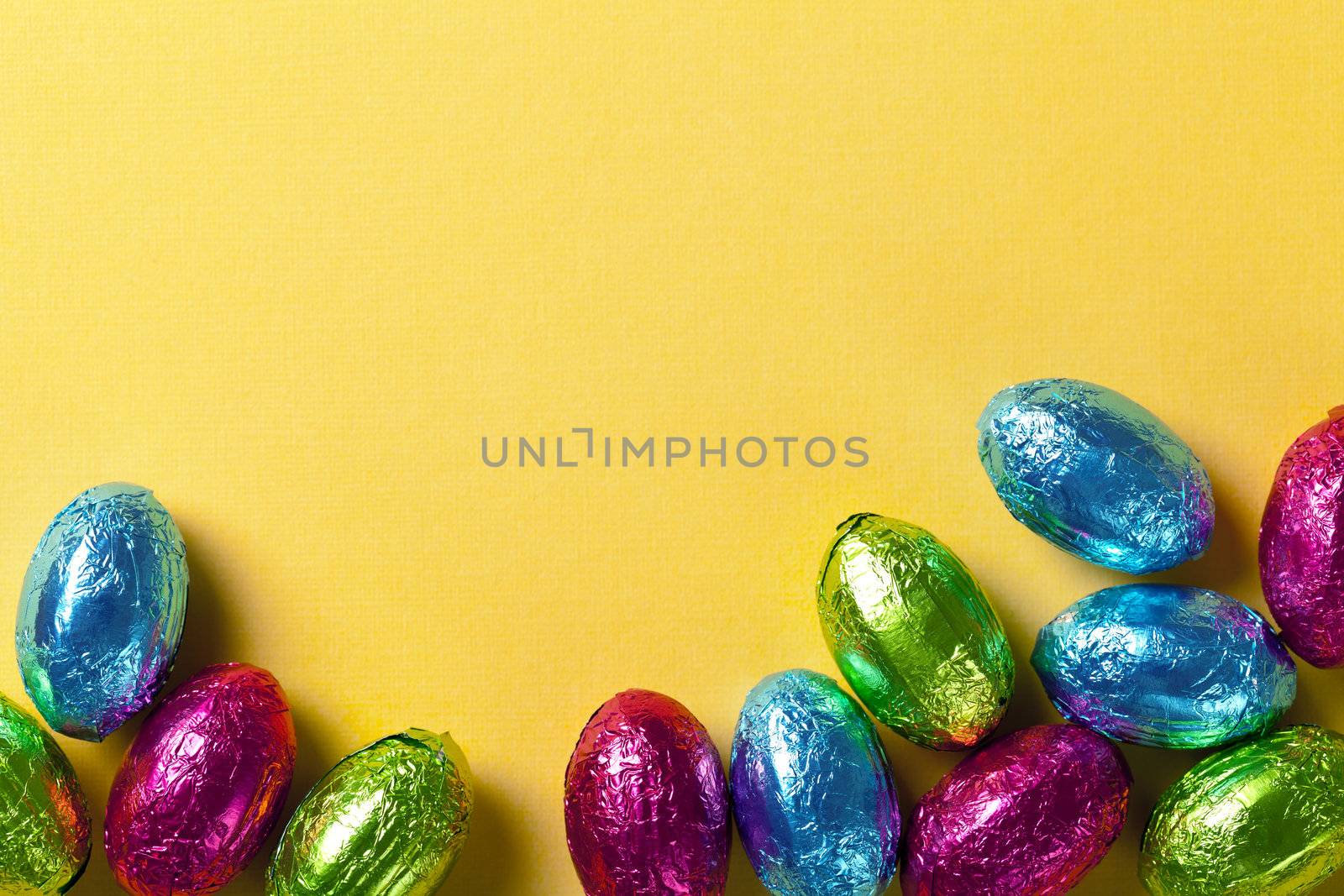 Easter background with colorful chocolate eggs on yellow paper. Top view, macro shot
