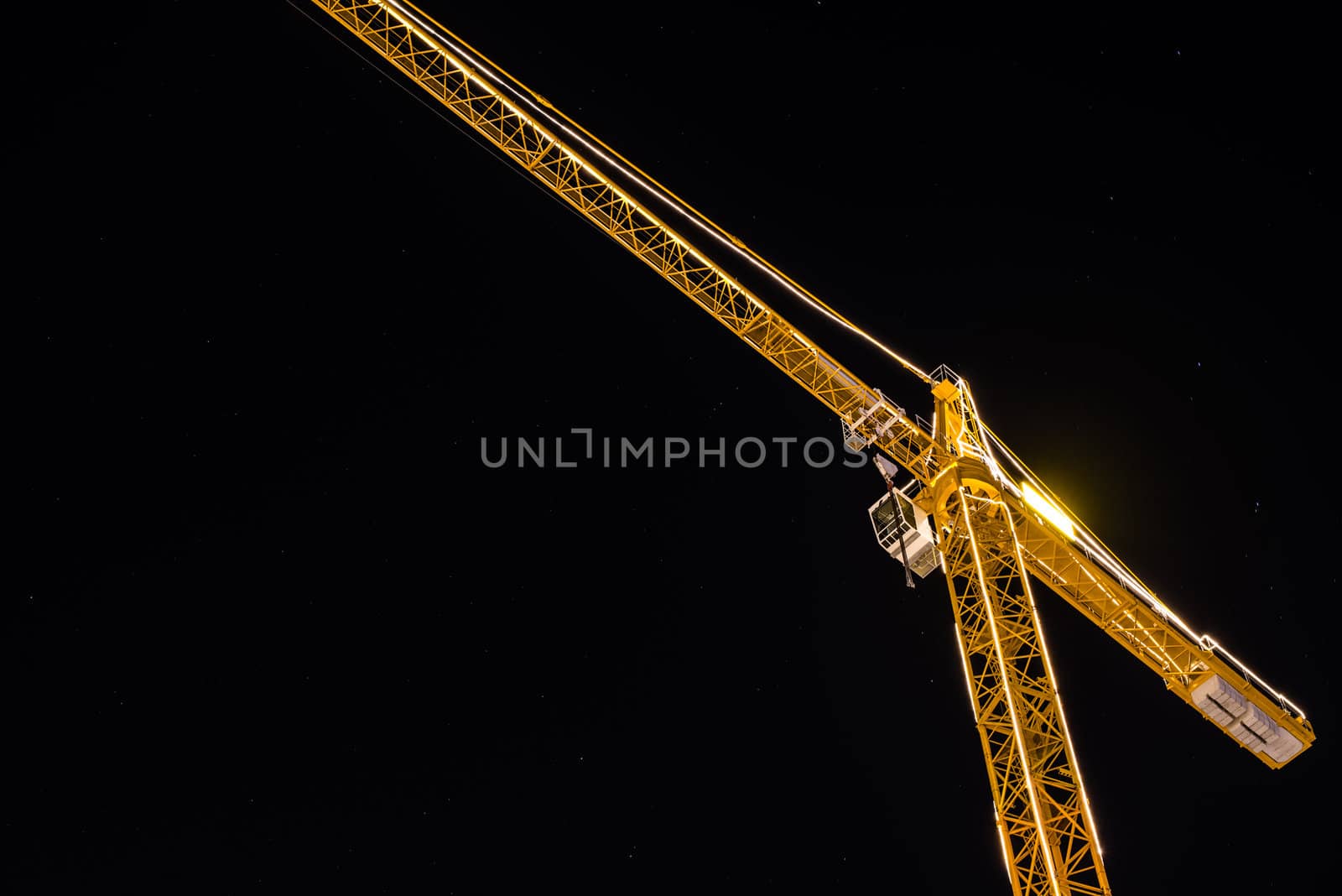 Construction crane at night brightly lit against stary sky