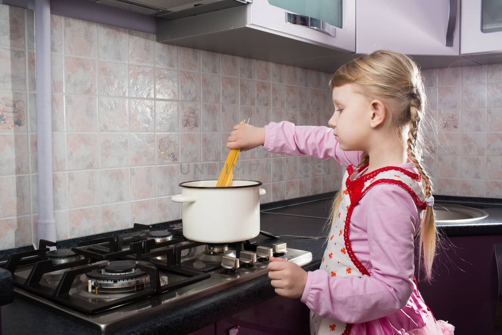 little girl in the kitchen putting pasta in the pot 