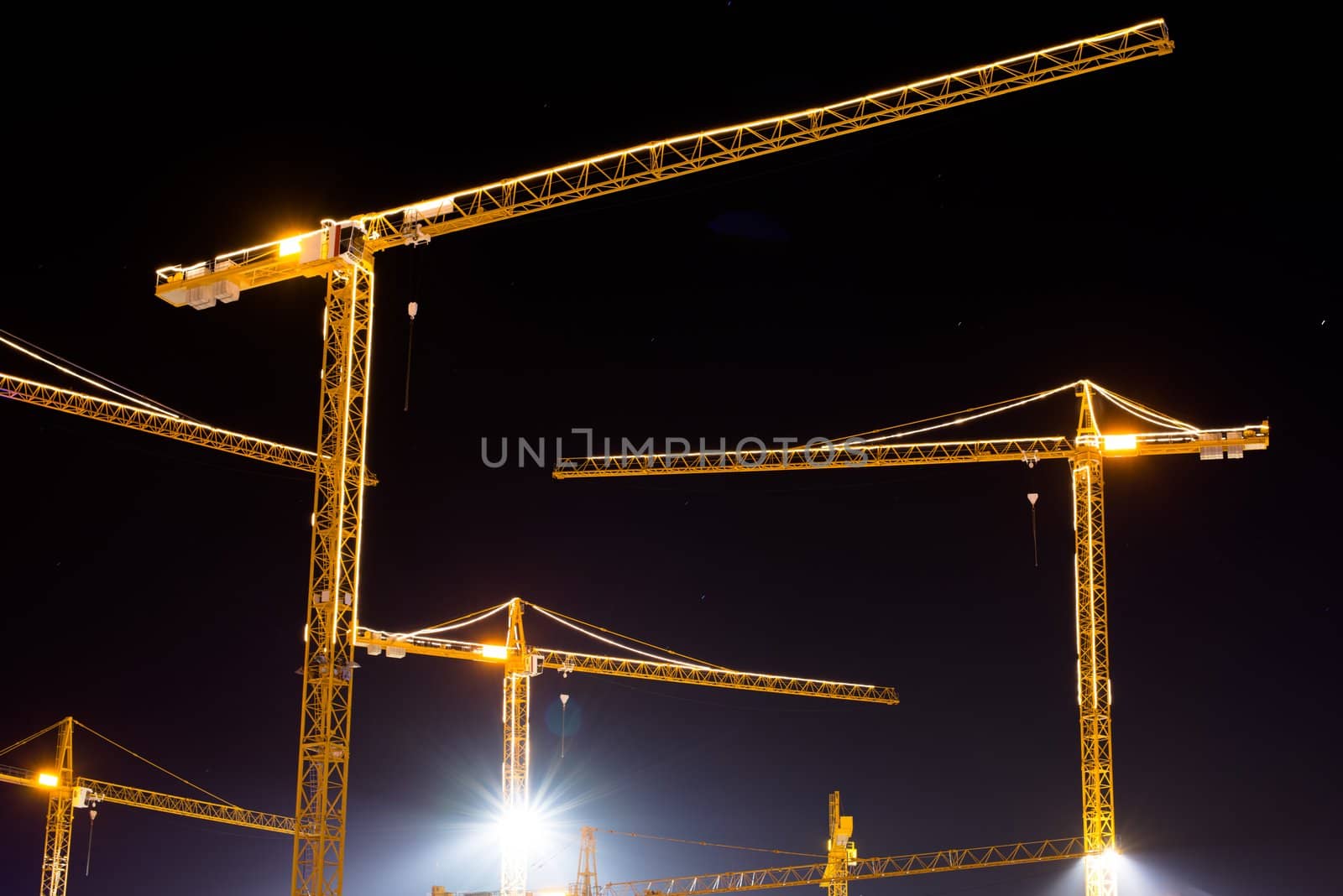 Construction cranes at night brightly lit against stary sky