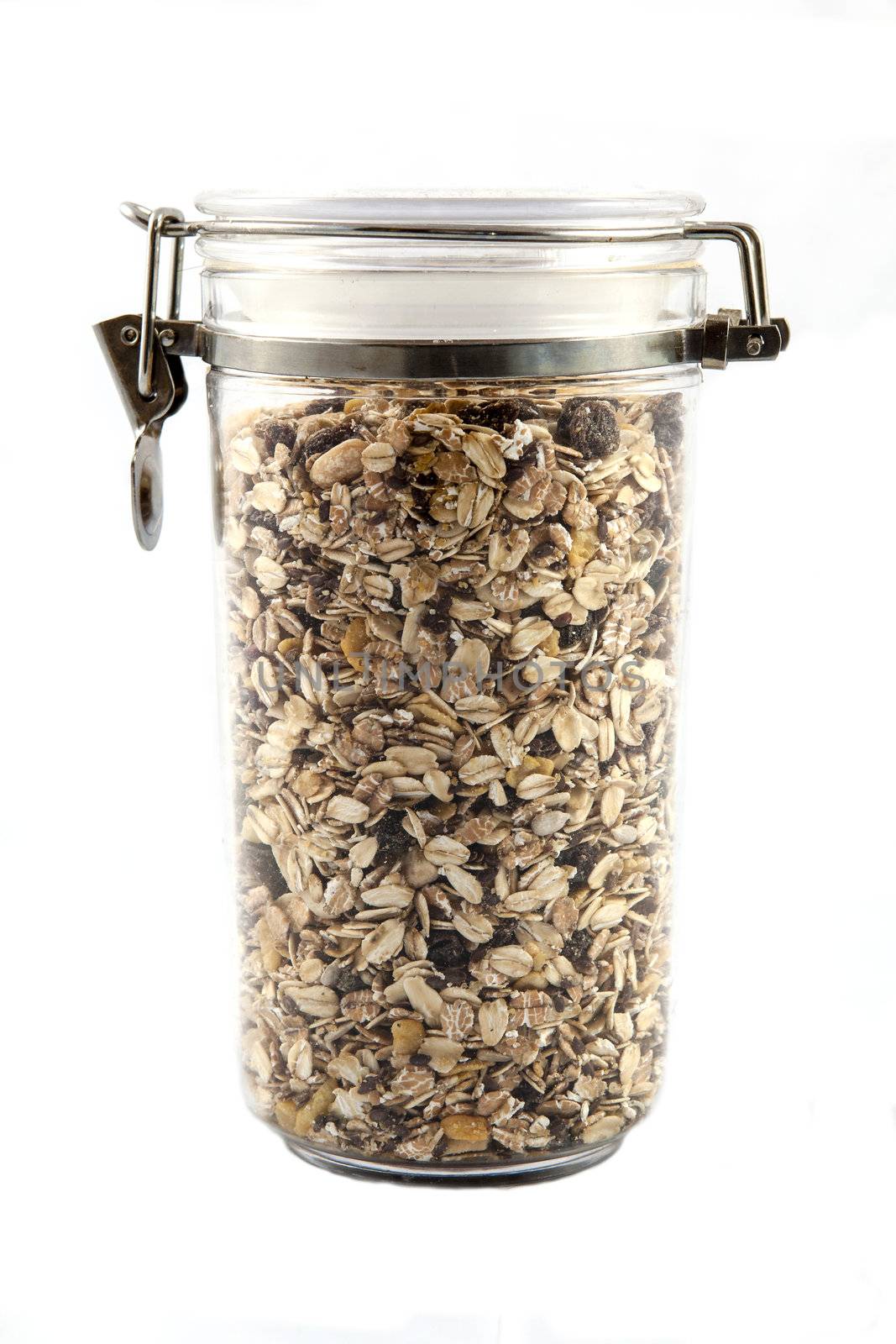 A transparent jar full of oats, fruits and nuts.