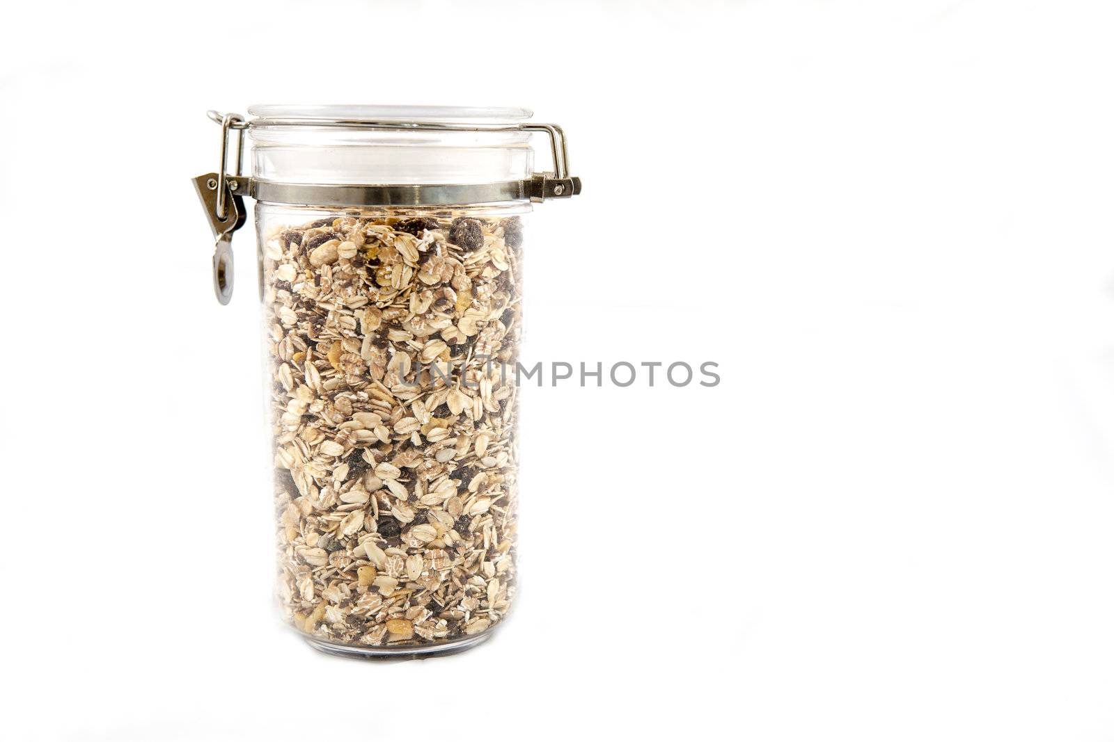 A transparent jar full of oats, fruits and nuts.