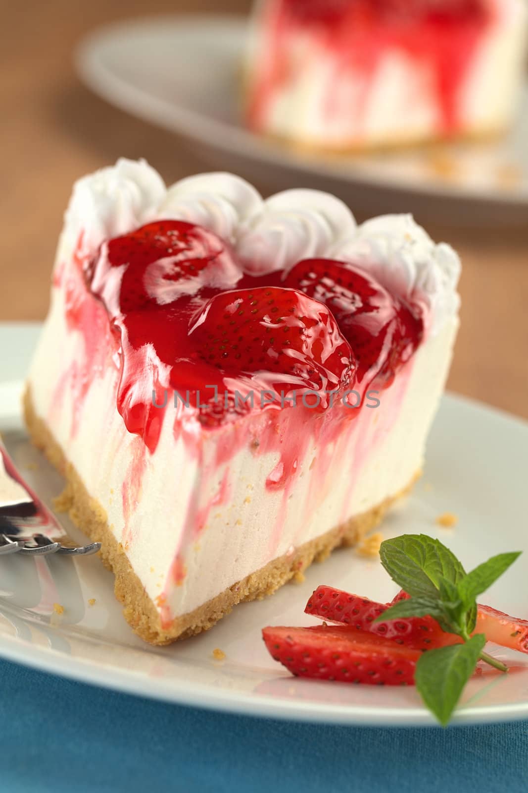 Fresh strawberry cheesecake with strawberry slices and mint on the side (Selective Focus, Focus on the first strawberry on the cake)