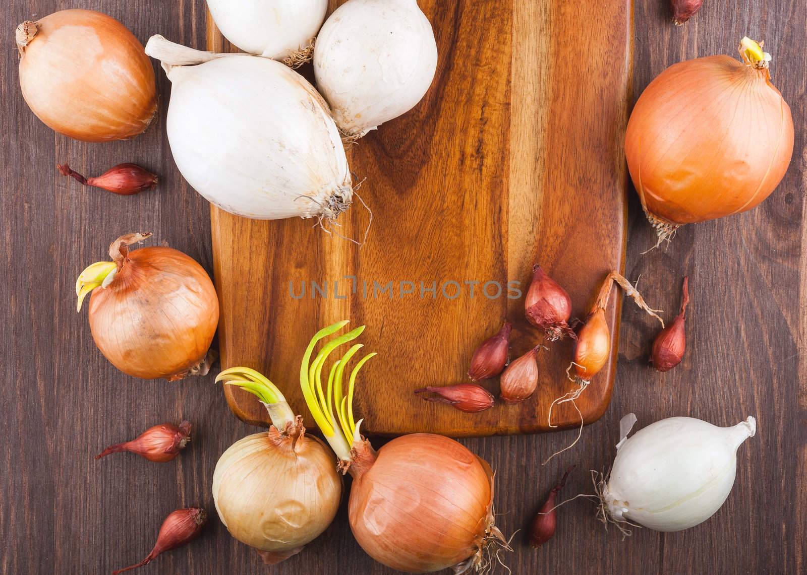 Different varieties of onions on a kitchen board and wooden surface