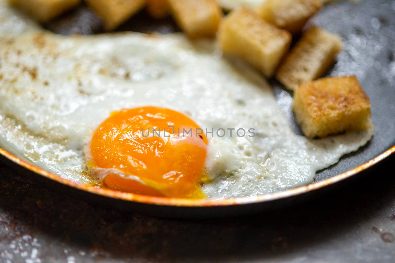 Frying pan full of scramble eggs from two eggs with a small pieces of toasted bread. Stands on grunge metal background.
