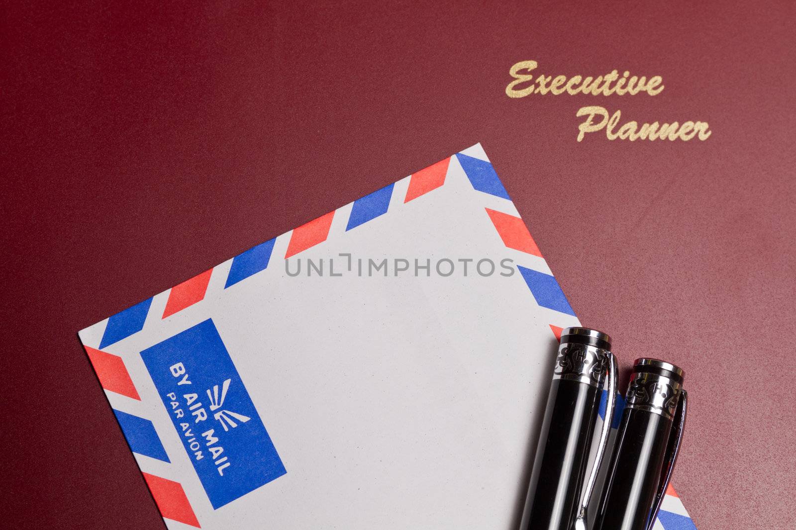 a brown executive planner with white envelope and two pens