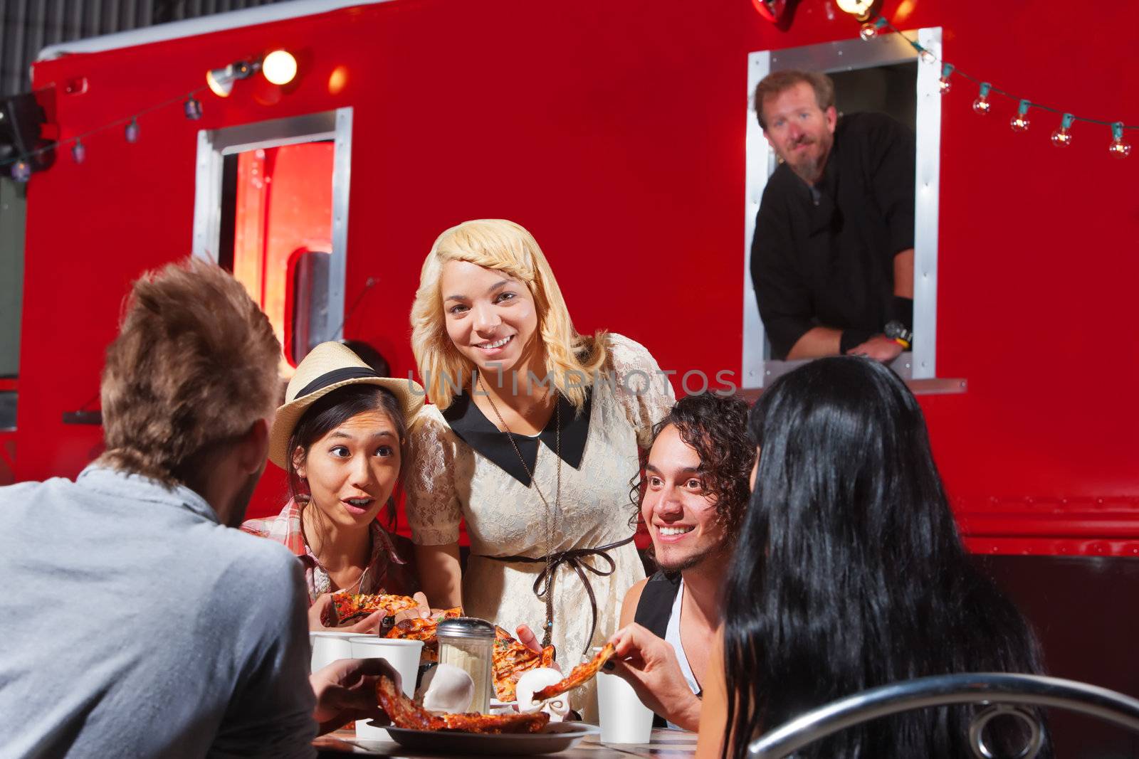 Happy group of friends eating out by food truck