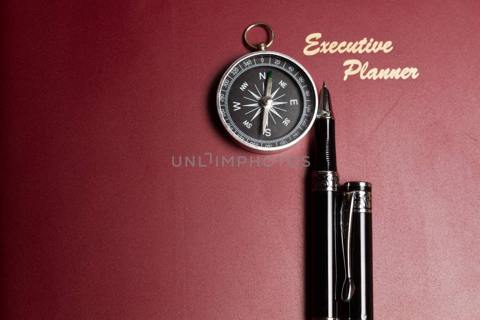 a dark red executive planner with a simple compass and two pens