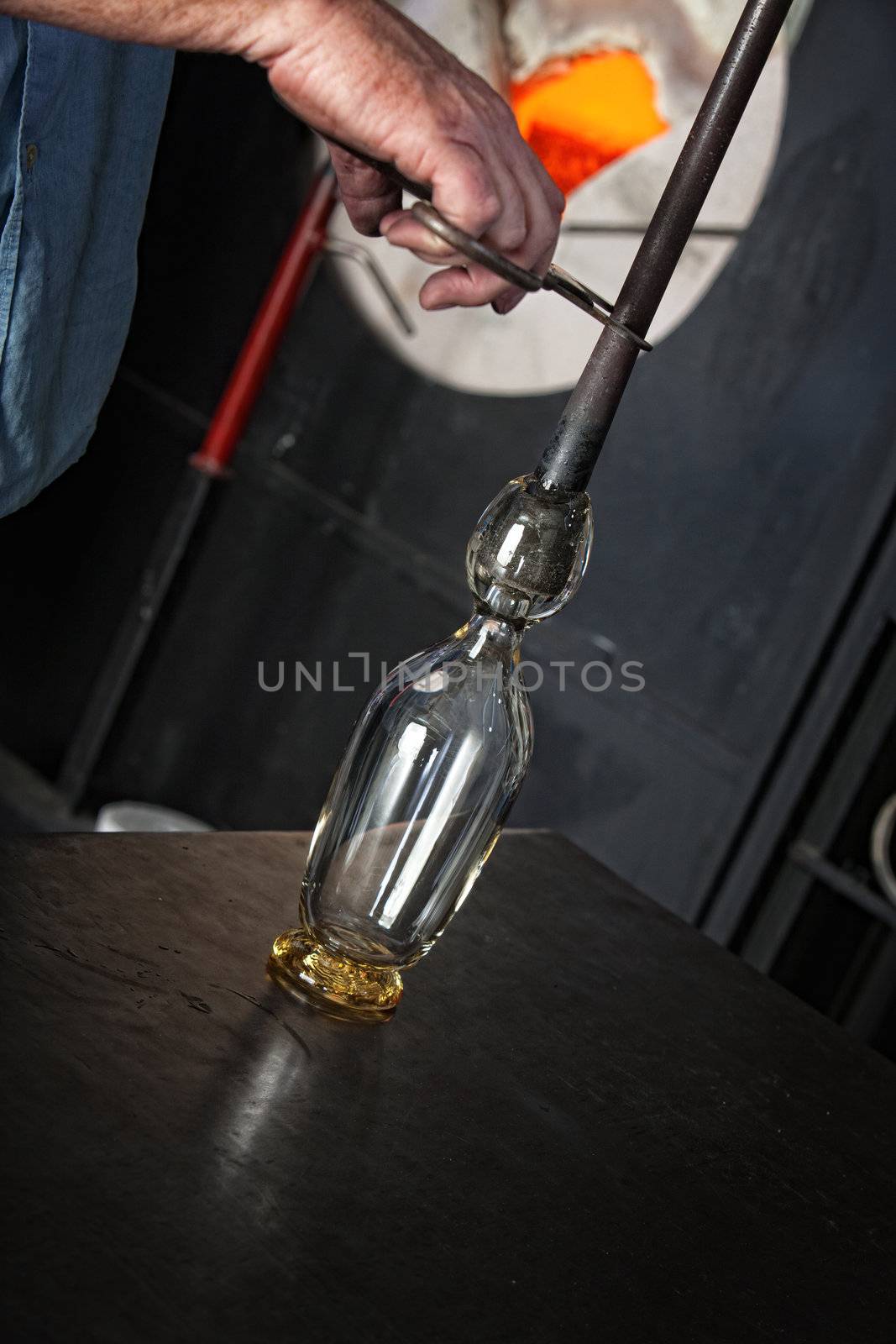Worker holding rod with hot glass on iron table