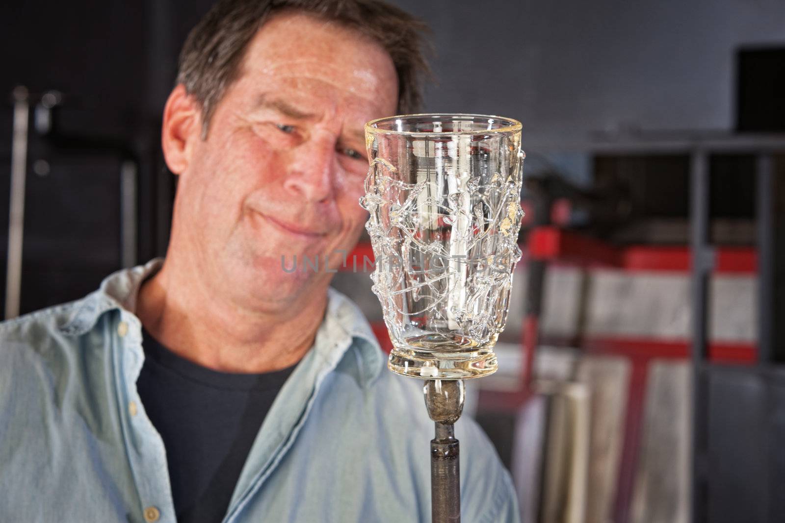 Proud man holding finished glass piece with iron rod