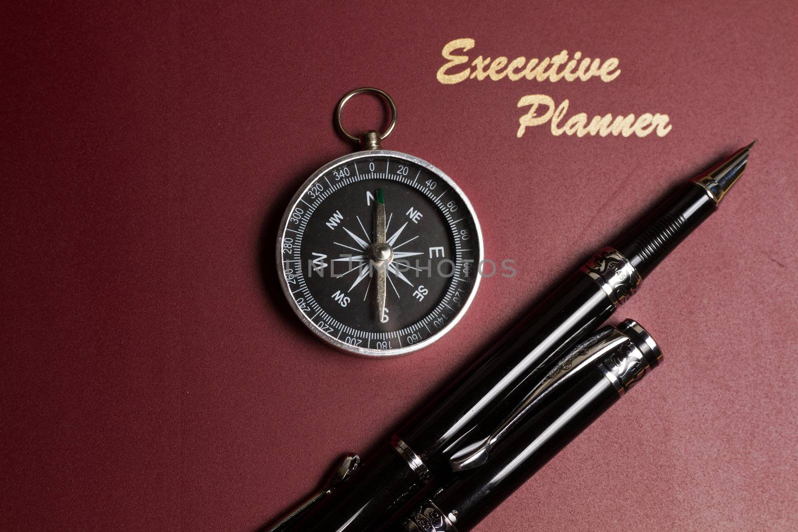 a dark red executive planner with a simple compass and two pens in landscape orientation