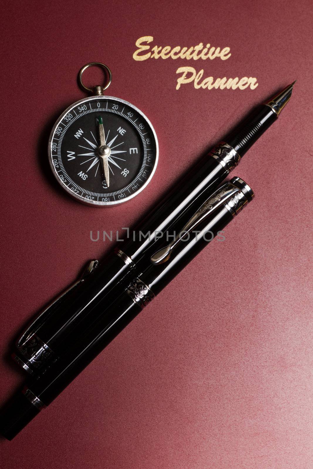 a dark red executive planner with a simple compass and two pens in portrait orientation