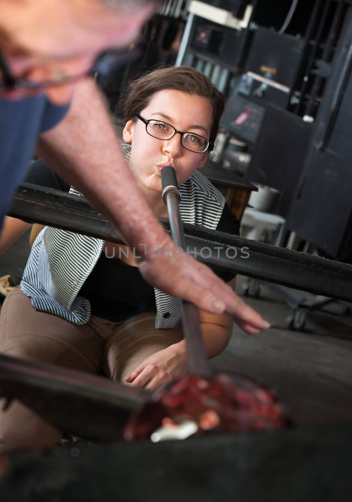 Man helping apprentice with blowing air to form glass