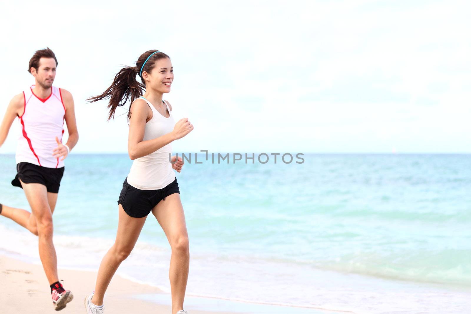 sport - couple running on beach training for marathon run. Young multiracial couple runners, smiling asian female fitness model and caucasian male model.