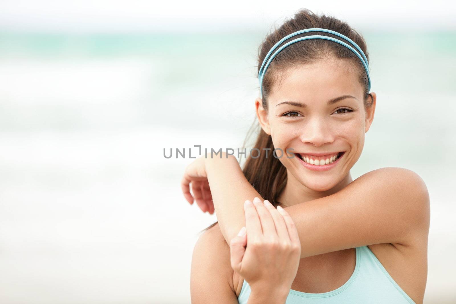 Fitness woman exercising smiling happy stretching out doing workout on beach. Beautiful mixed race Asian Caucasian female fitness model portrait.