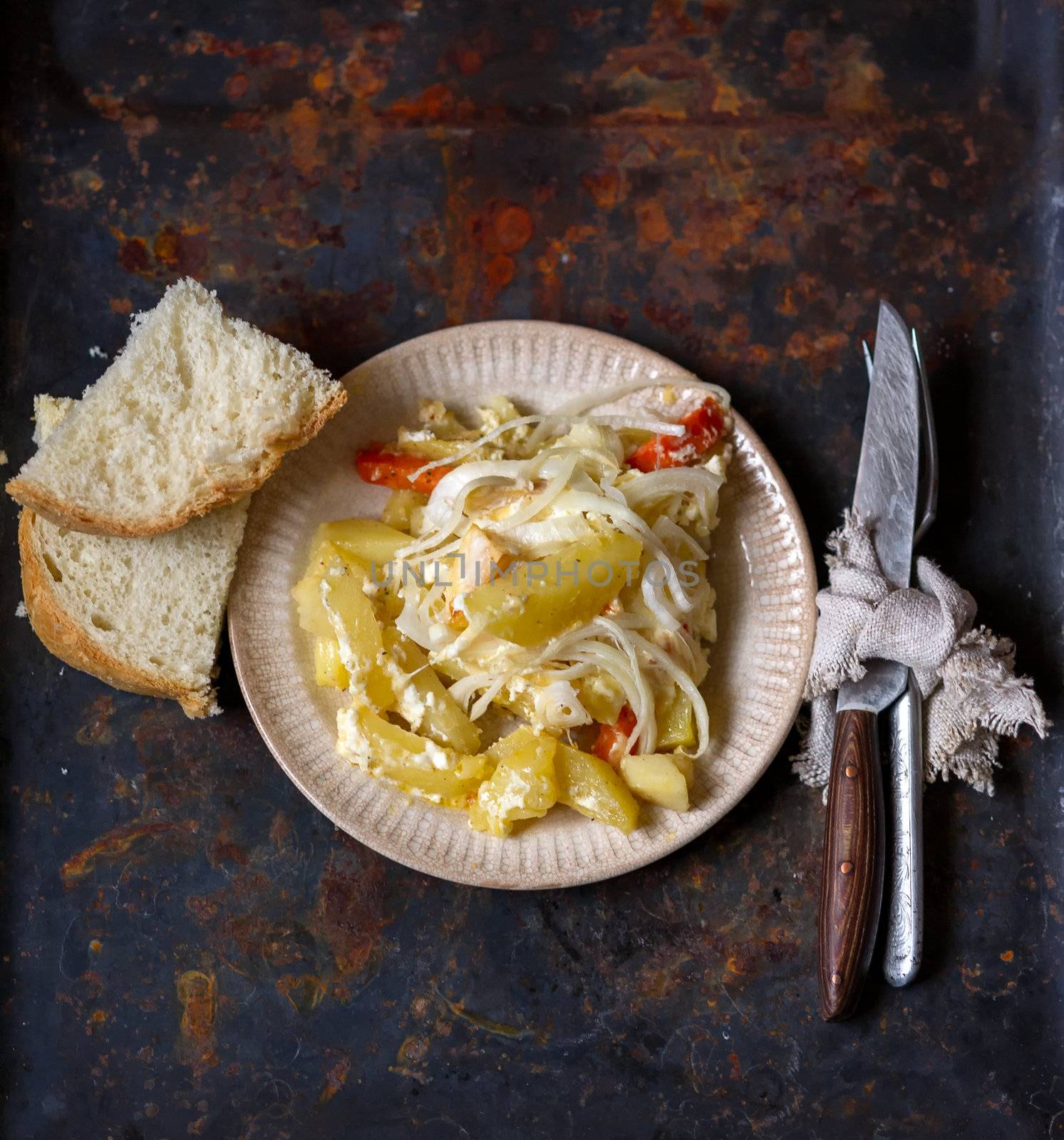 Still of potatoes and onion baked served with sliced bread, fork and knife on dark rusty metal background