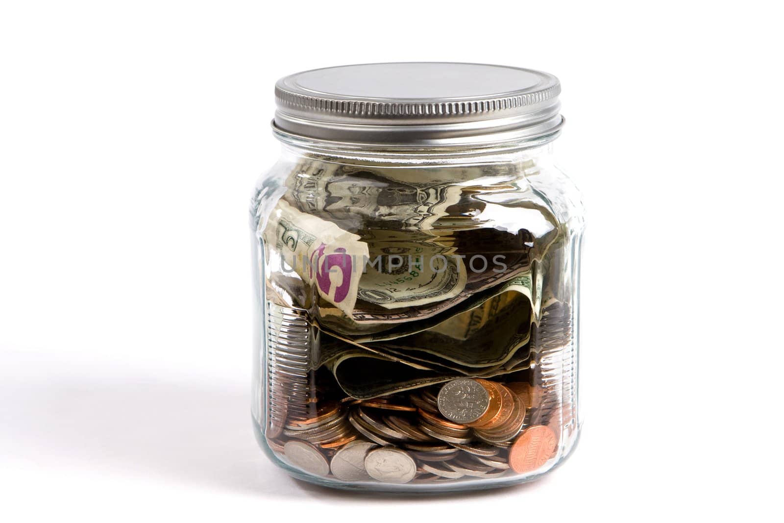 Clear glass jar filled with USA dollars and coins sit on a white background financial concept.