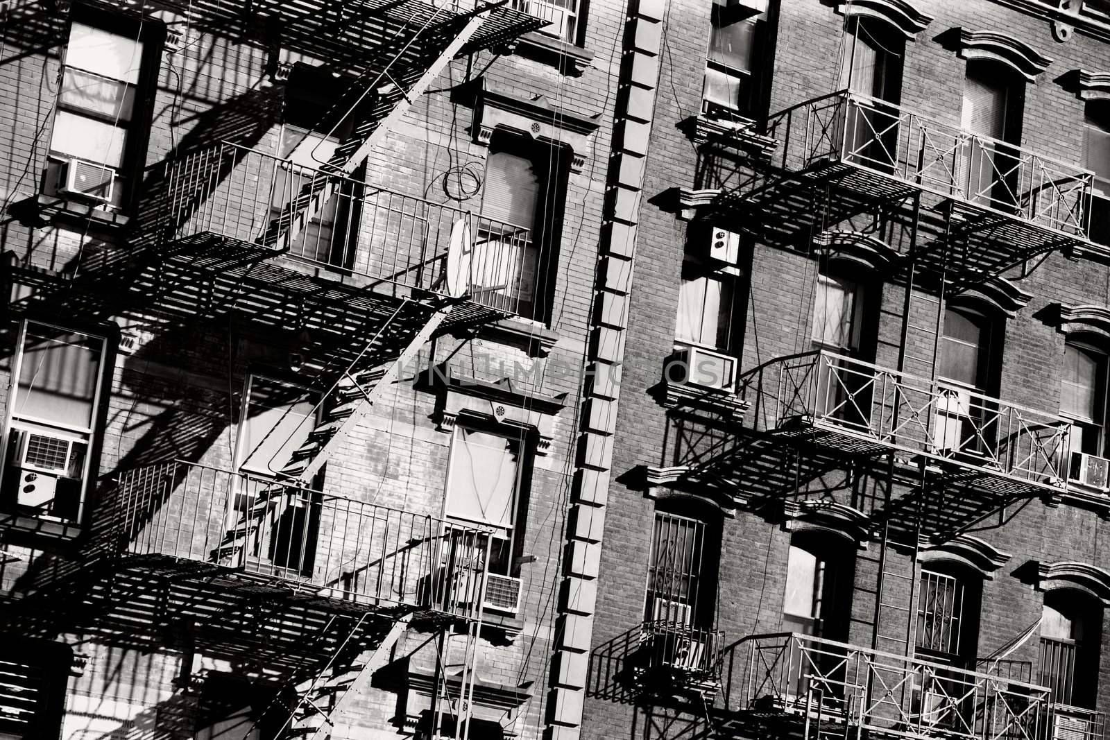 Black and white photo of the exterior of a building in New York with old fire escape.
