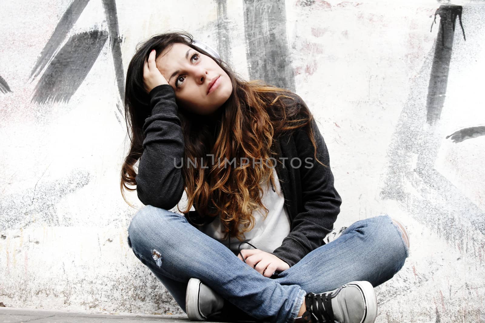 A young woman listening to melancholic Music and sitting on the pavement.