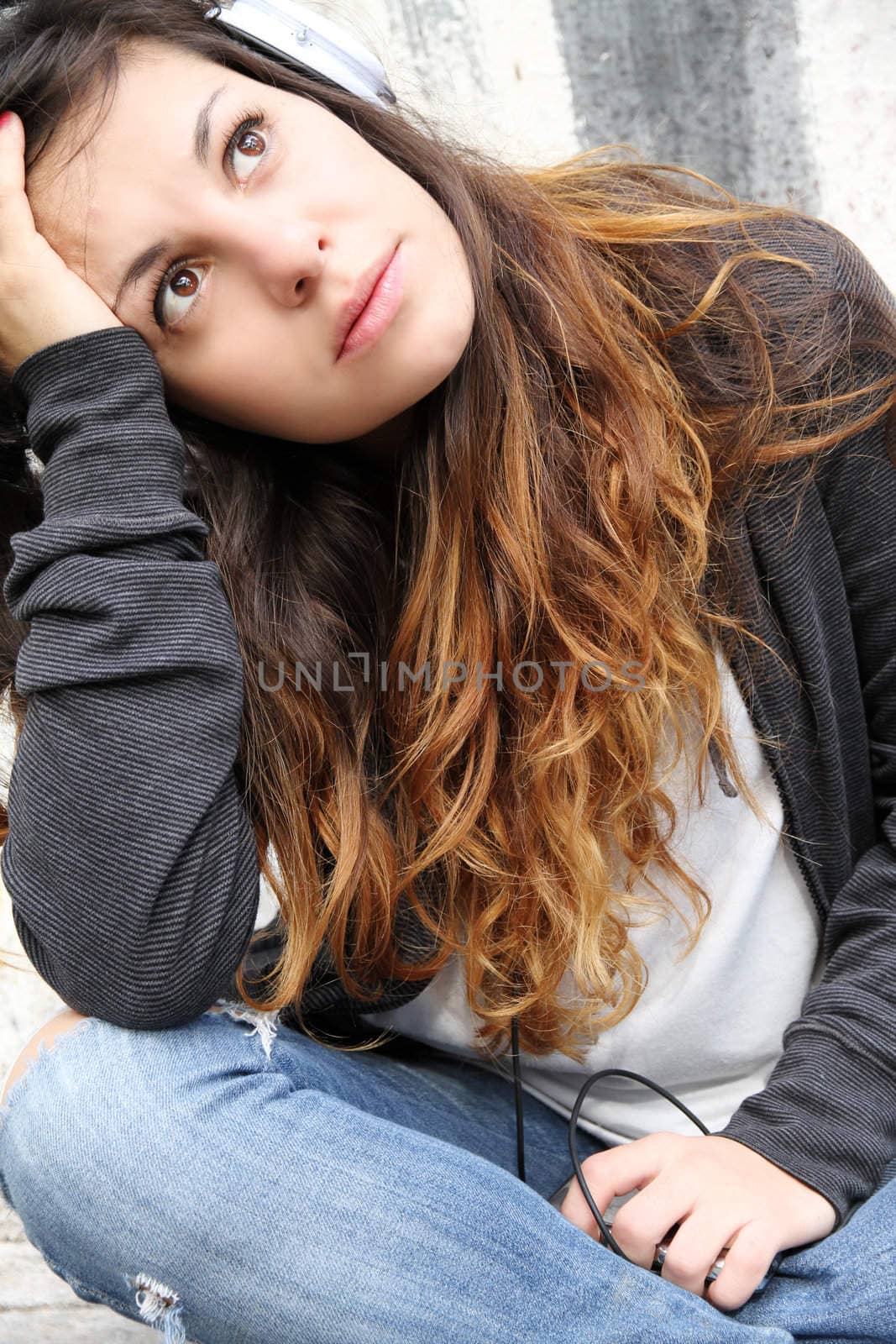 A young woman listening to melancholic Music and sitting on the pavement.