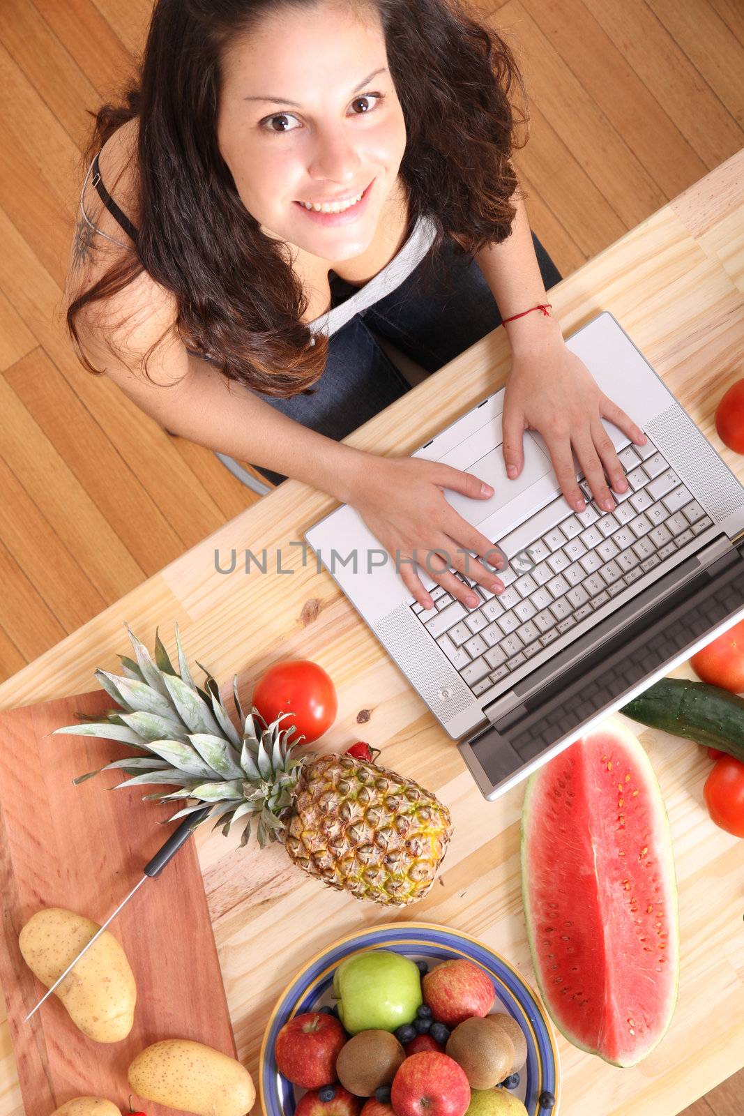A young woman using a Laptop while cooking.