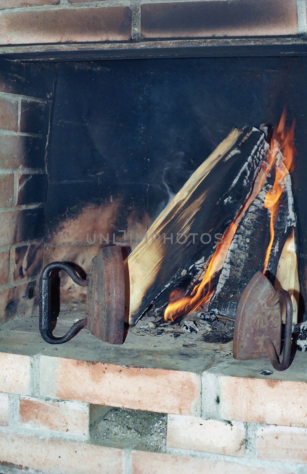 Two old irons in fireplace near burning wood