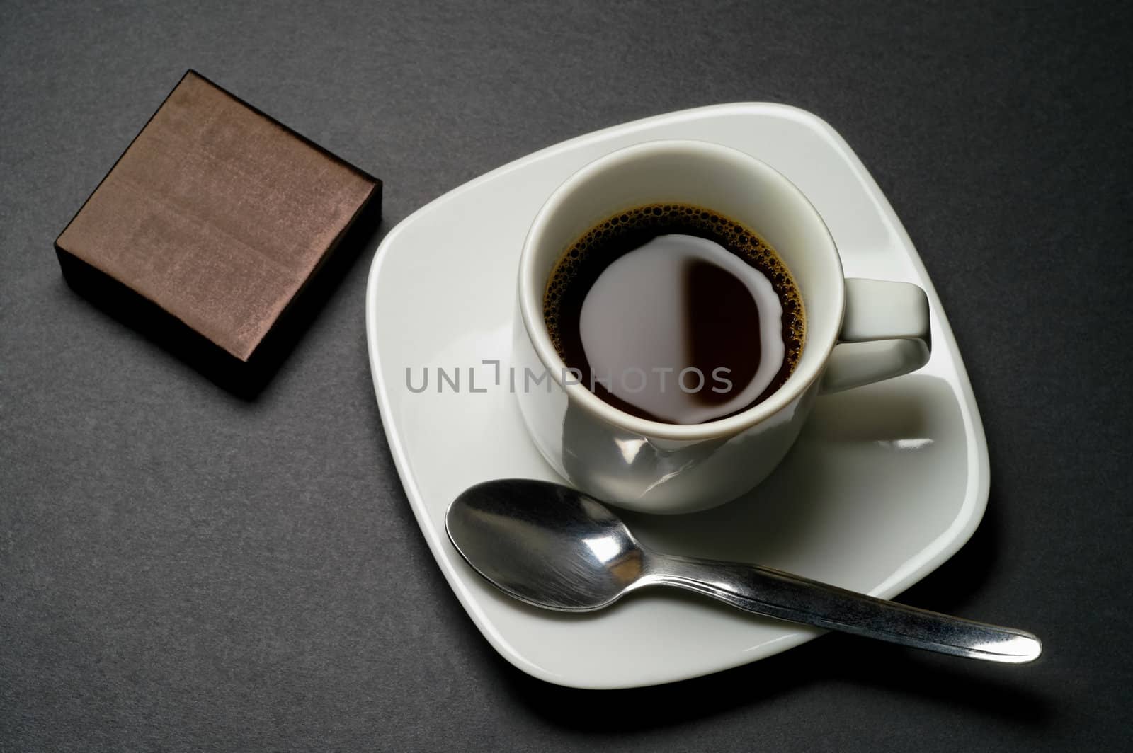 Coffee cup with wrapped chocolate, biscuit, etc.  on dark grey background closeup