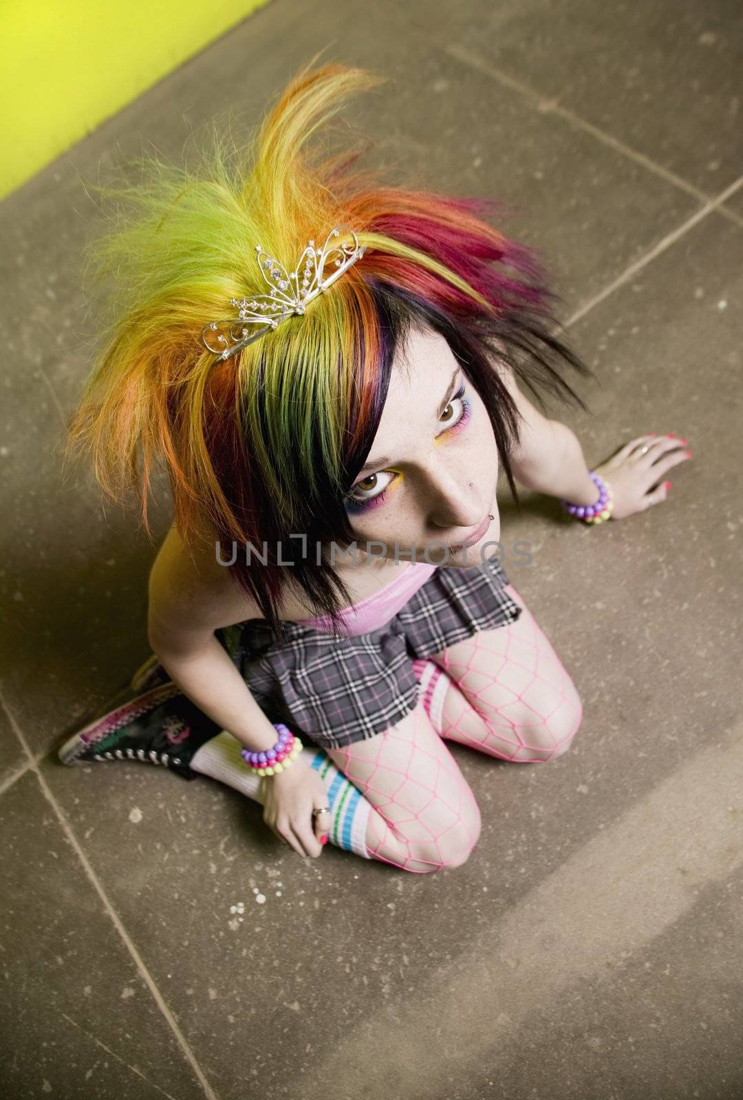 Colorful young punk girl sitting in front of a green wall