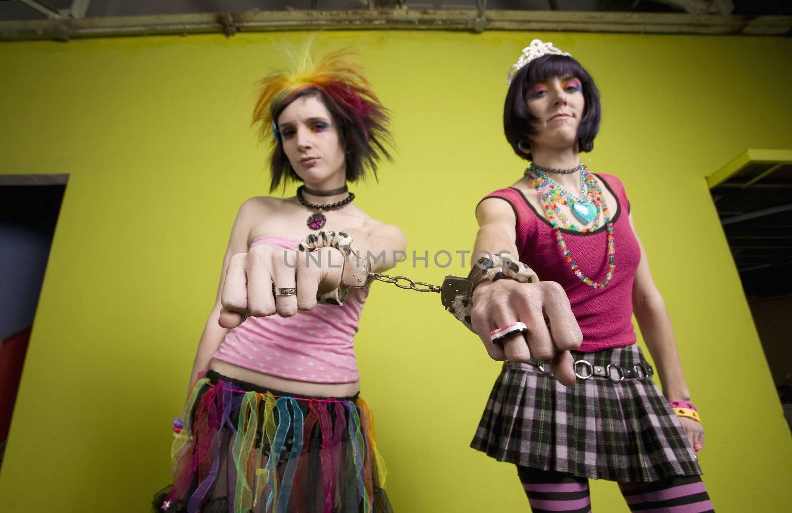 Wide angle of young punk women in front of a green wall linked by handcuffs