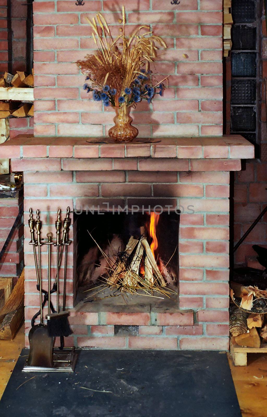 Village fireplace with fire irons and dead flowers on mantelshelf
