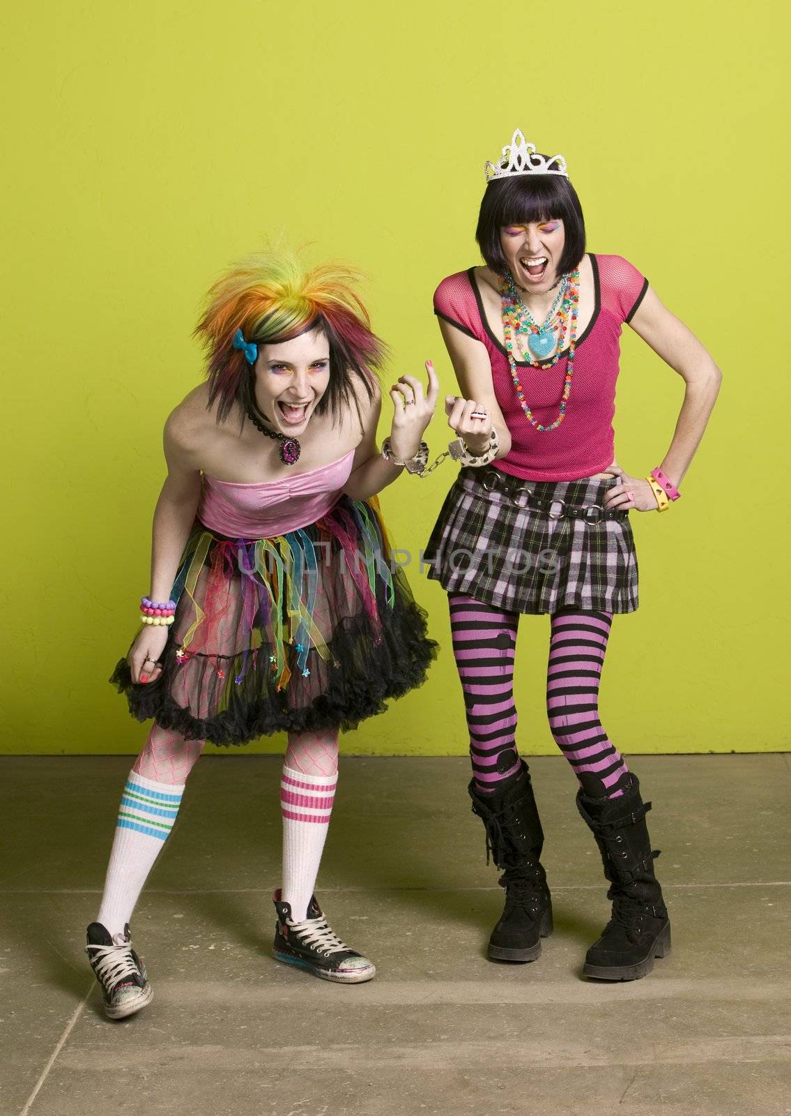 Young punk women in front of a green wall linked by handcuffs