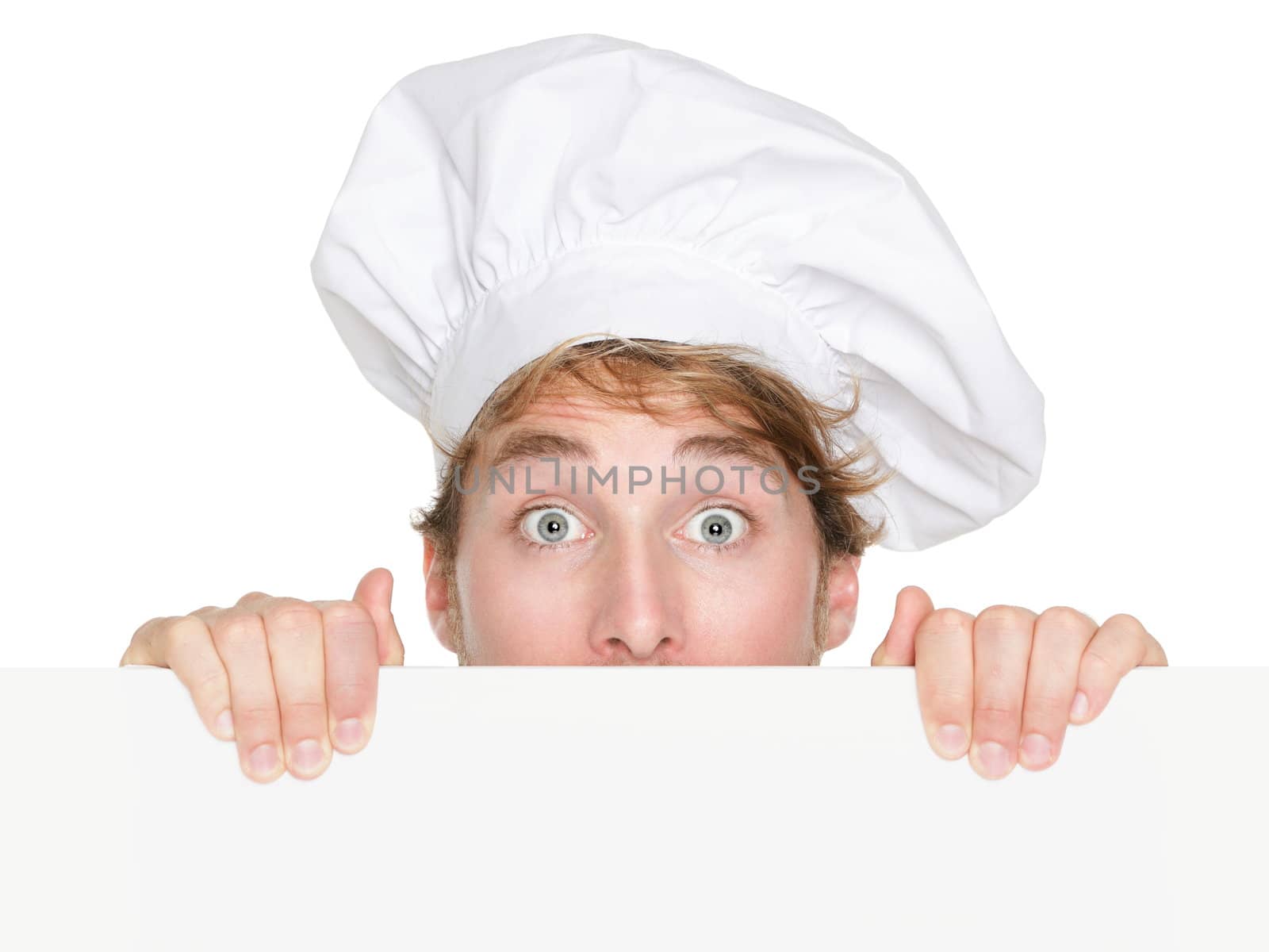 Chef sign. Man chef, cook or baker peeking up holding blank white paper sign with copy space for text or menu. Young Caucasian male chef looking funny surprised isolated on white background.
