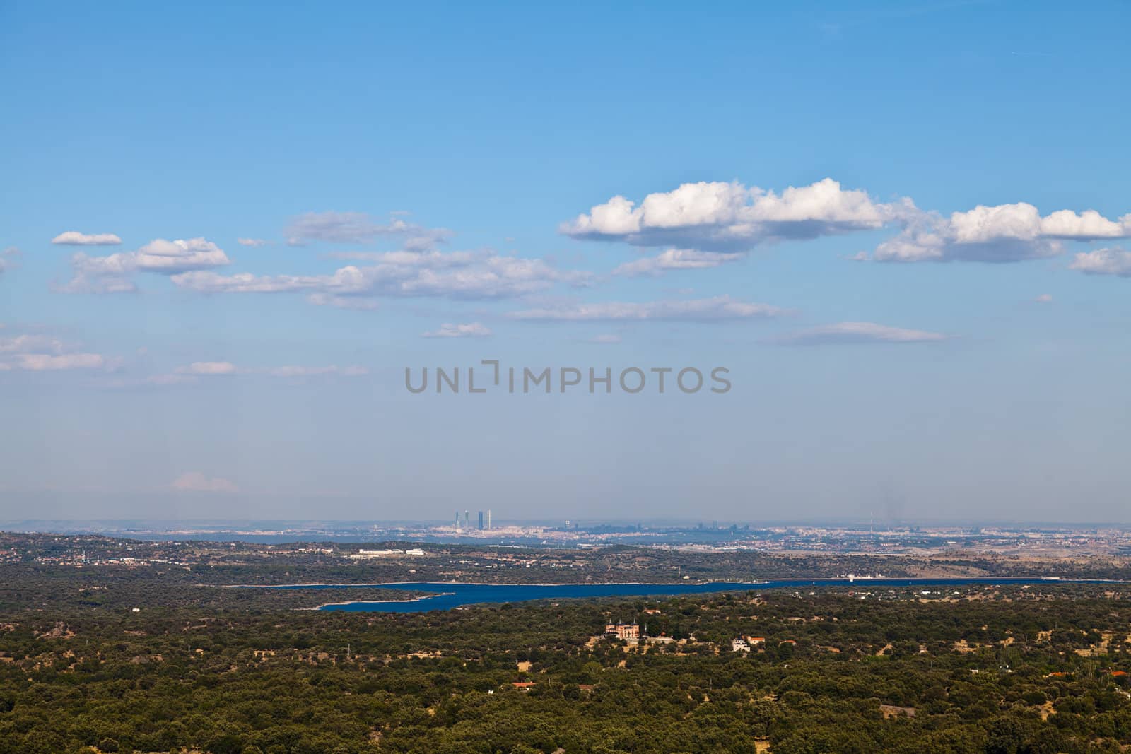 View of the city of Madrid from a distance. Bright blue lake in the foreground. Taken on a sunny day with bright blue sky and a few white clouds.