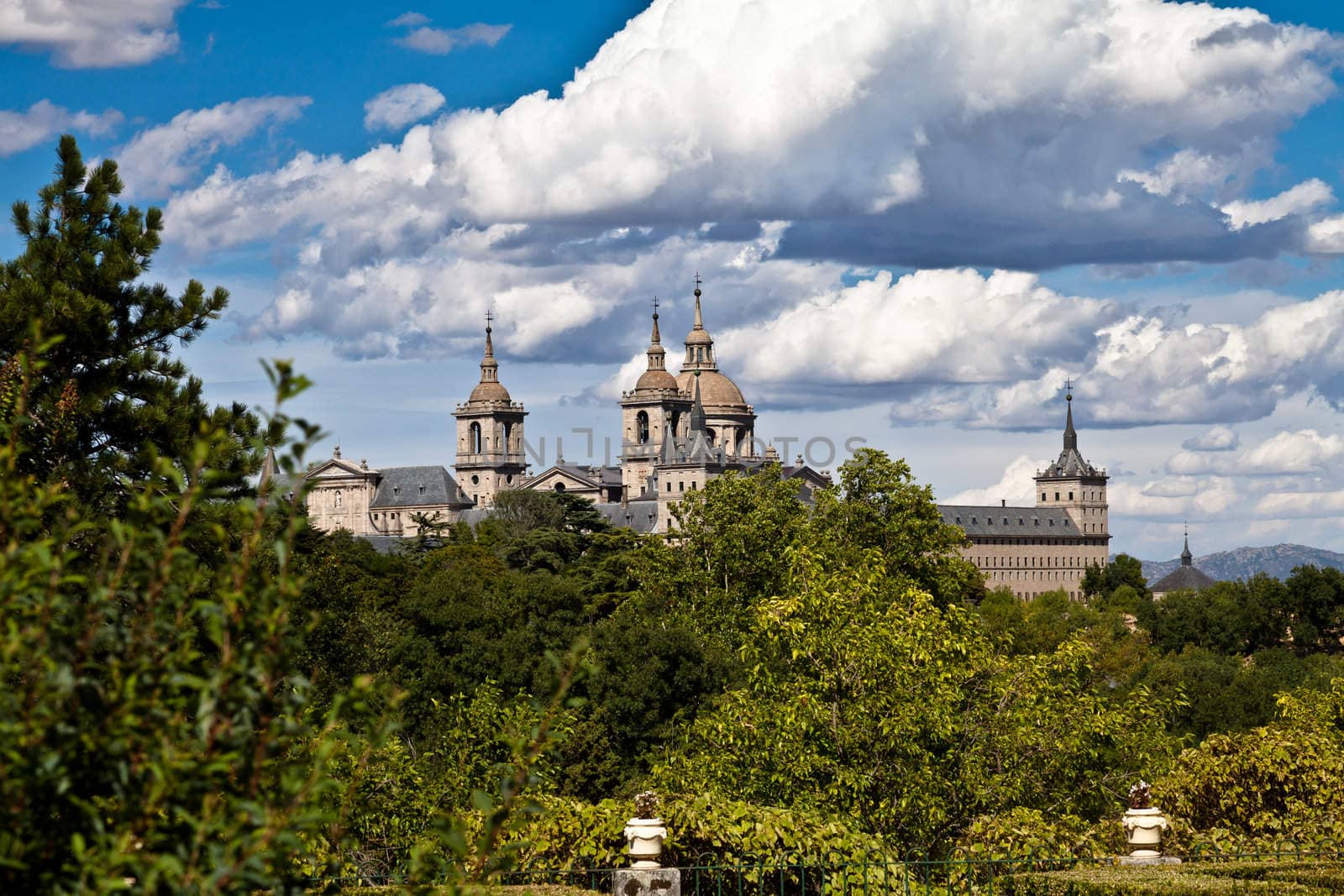 San Lorenzo de El Escorial Monastery from Casita del Infante. The towers of the church and monastery are set of by a bright blue sky.