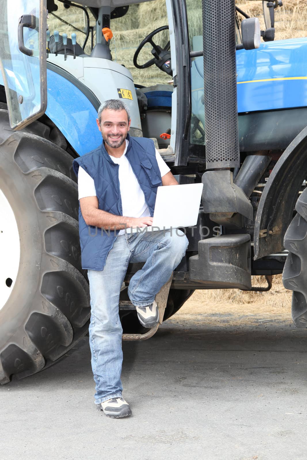 Famer with laptop computer stood by tractor by phovoir
