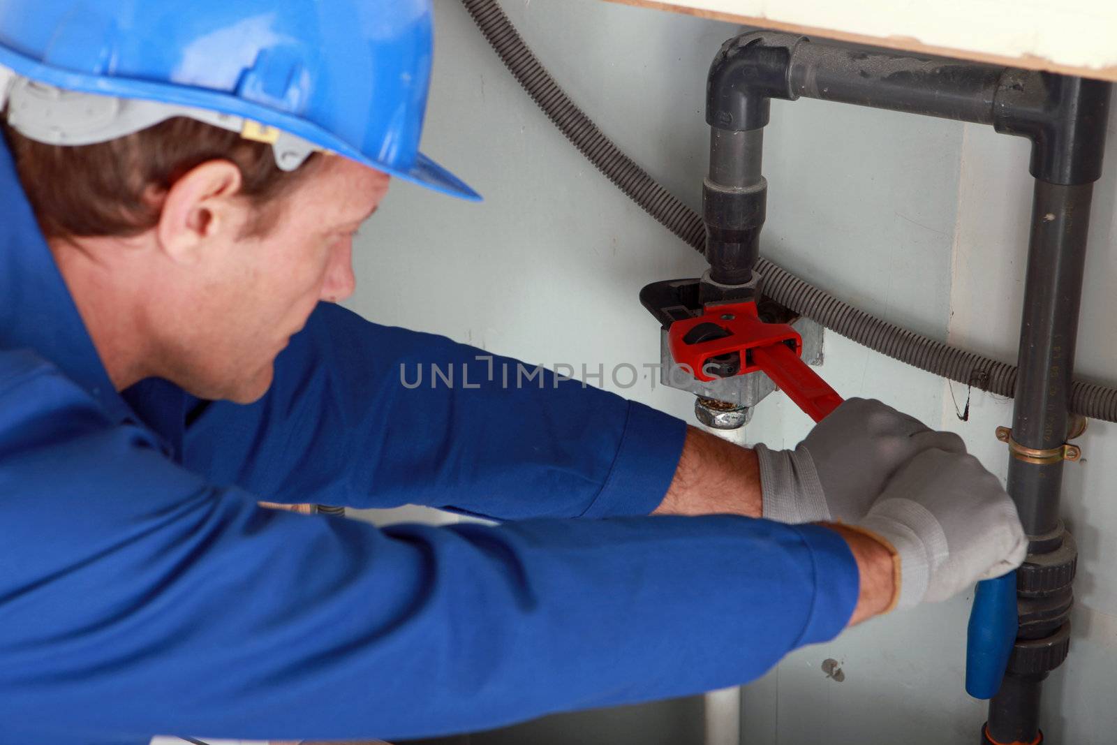 Man using a large red wrench on some interior water pipes by phovoir