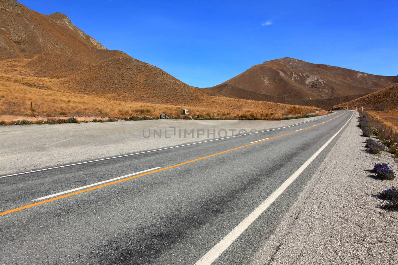 Long road stretching out to  dry mountain range at Lindis Pass, the highest highway, in NewZealand