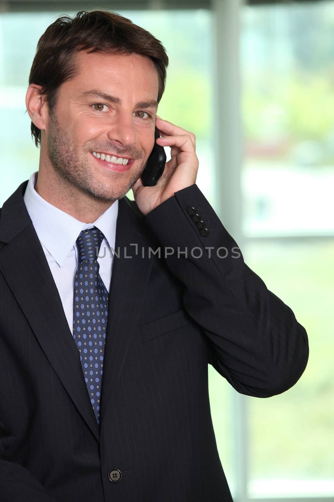 Smiling businessman using a telephone by phovoir