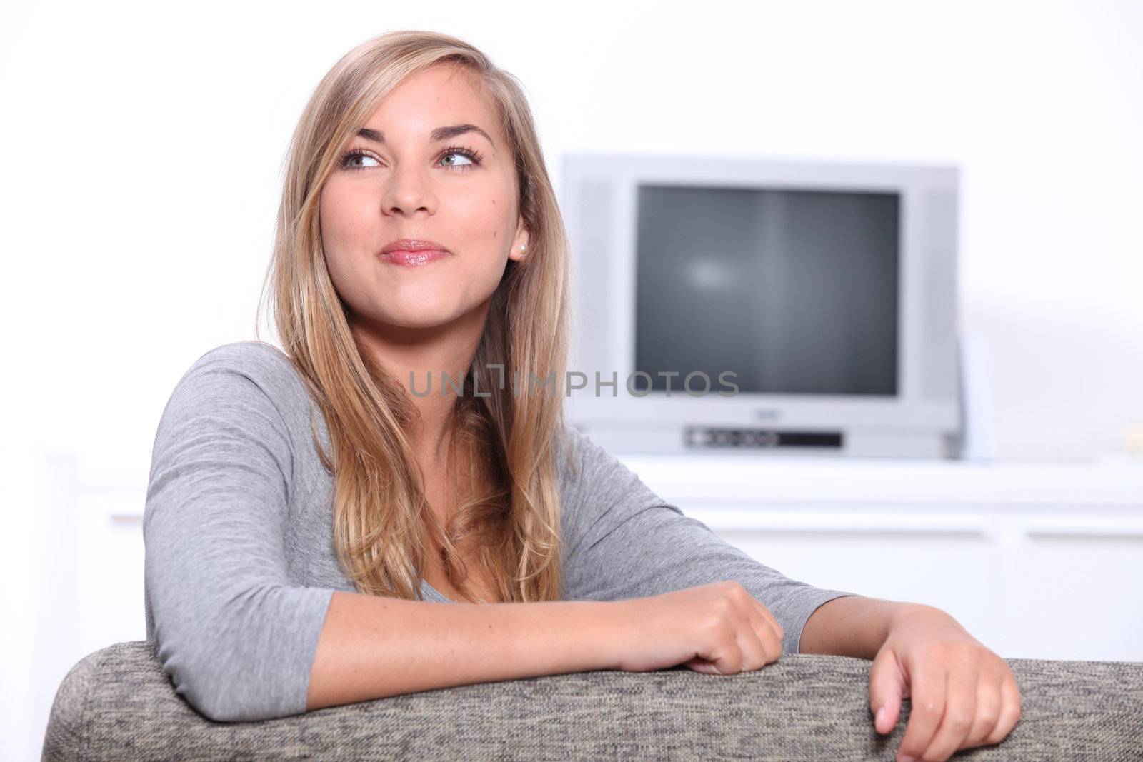 Smiling young woman sitting on a couch with a television set in the background by phovoir