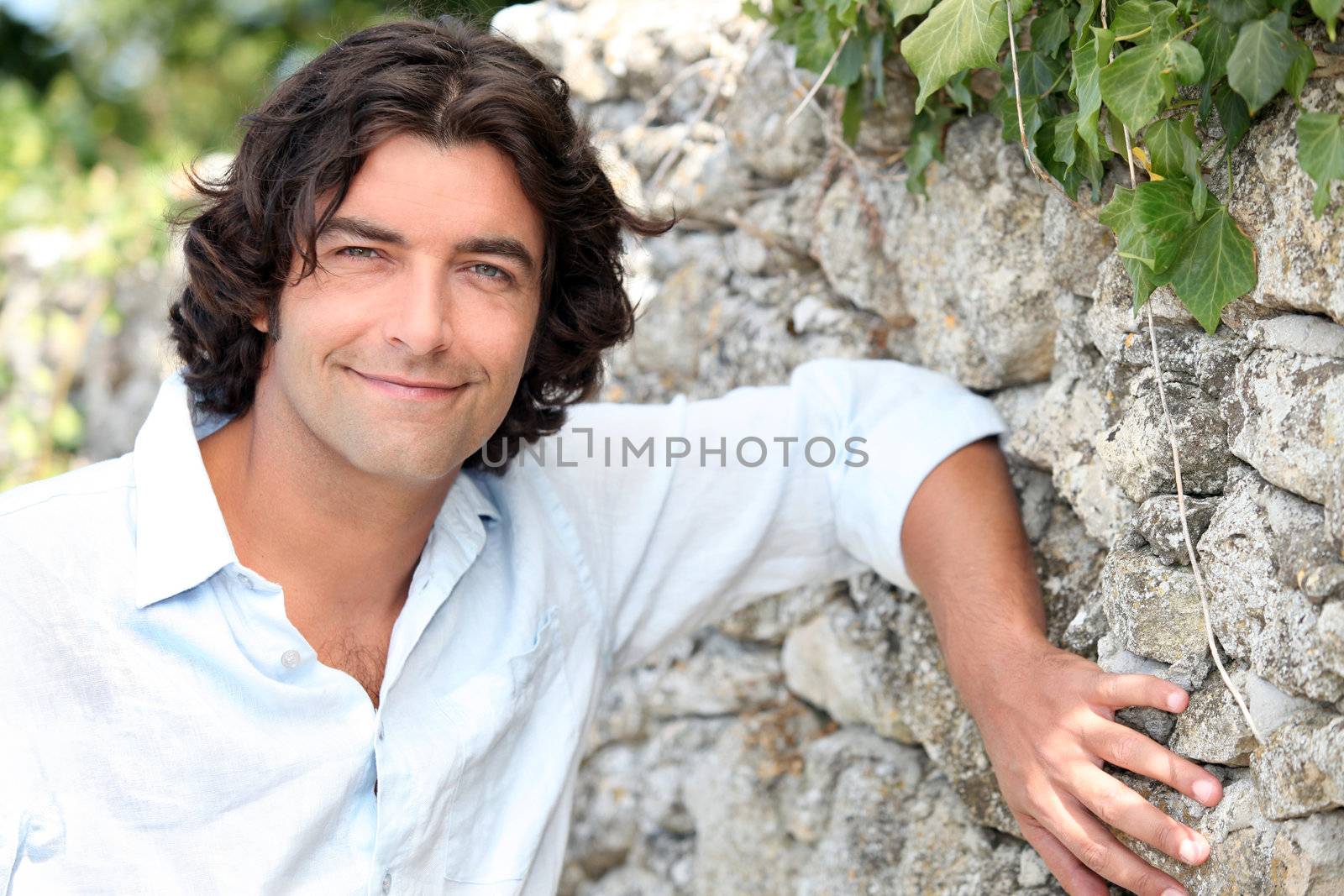 Good looking man leaning against an old stone country wall by phovoir
